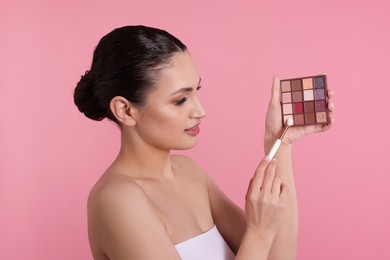 Photo of Woman with eyeshadow palette and brush on pink background