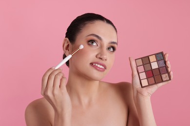 Photo of Woman with eyeshadow palette and brush applying makeup on pink background