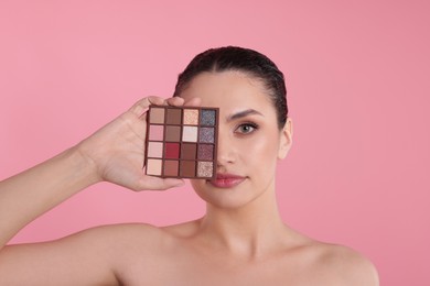 Photo of Woman covering eye with eyeshadow palette on pink background
