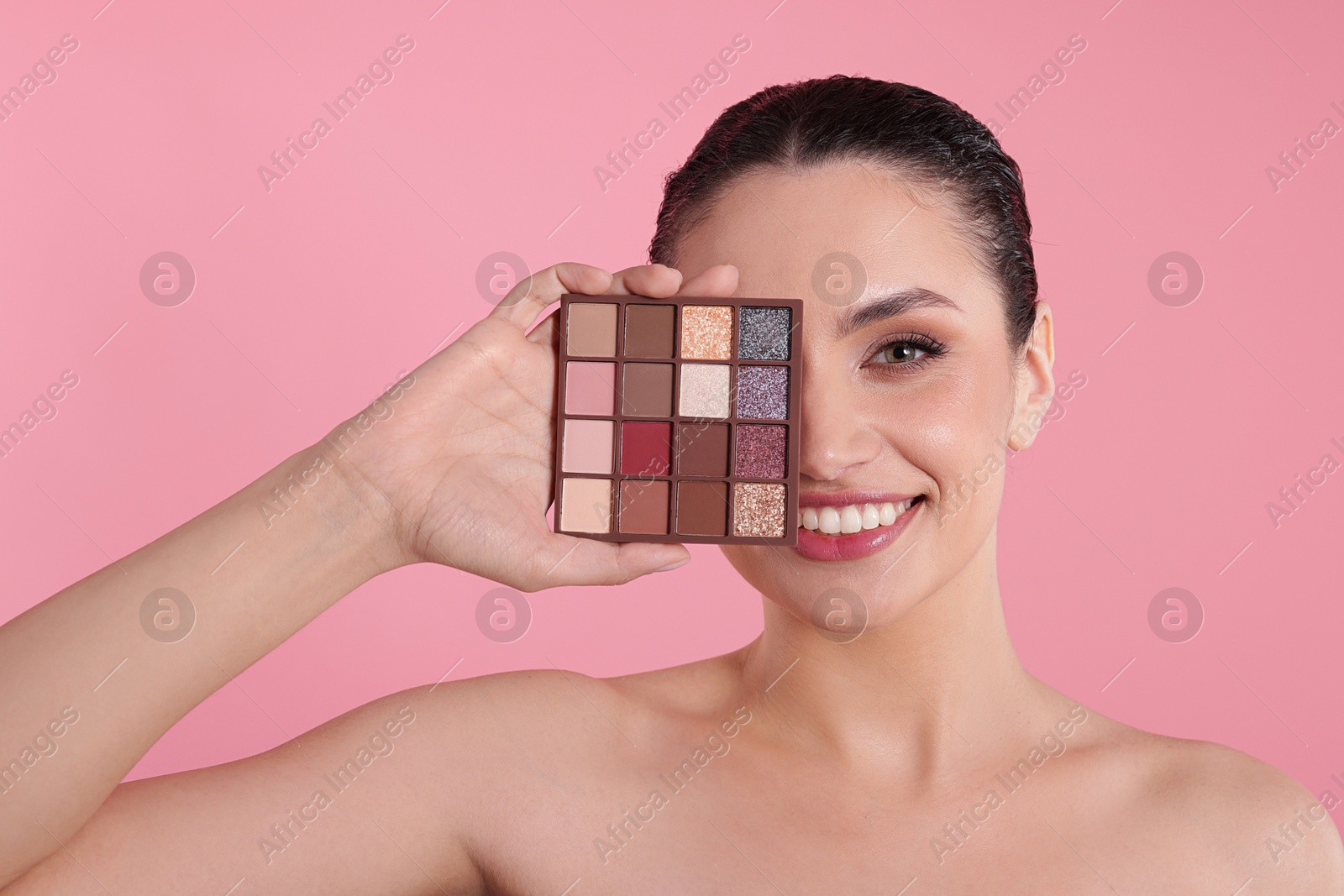 Smiling woman covering eye with eyeshadow palette on pink background Photo of Smiling woman covering eye with eyeshadow palette on pink background