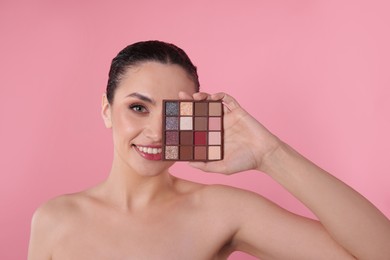 Photo of Smiling woman covering eye with eyeshadow palette on pink background