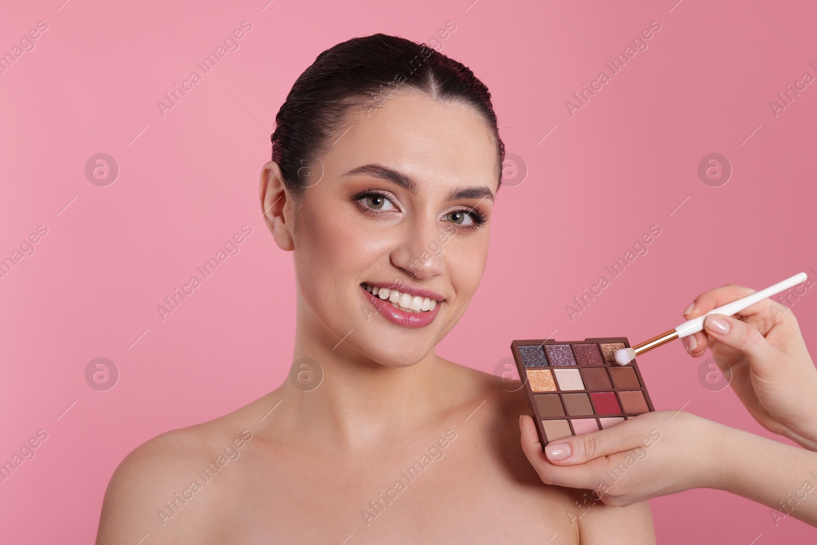 Makeup artist with eyeshadow palette, brush and smiling woman on pink background, closeup Photo of Makeup artist with eyeshadow palette, brush and smiling woman on pink background, closeup