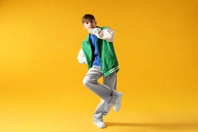 Photo of Boy in stylish clothes dancing on orange background