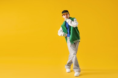 Photo of Boy in stylish clothes dancing on orange background, space for text