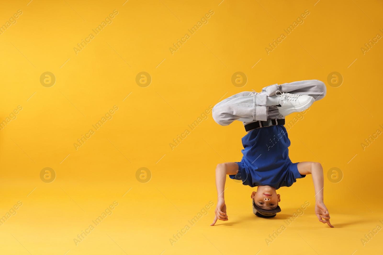 Photo of Boy in stylish clothes dancing on orange background, space for text