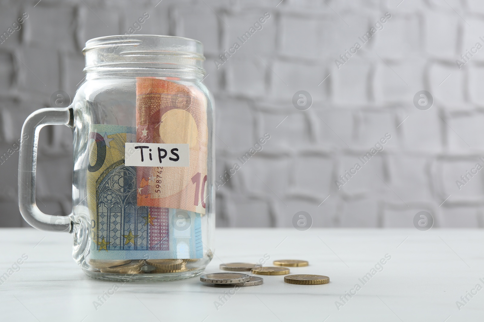 Tips jar with money on white marble table, space for text Photo of Tips jar with money on white marble table, space for text