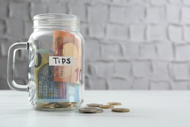 Photo of Tips jar with money on white marble table, space for text