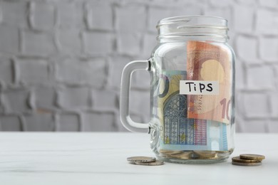 Photo of Tips jar with money on white marble table, space for text