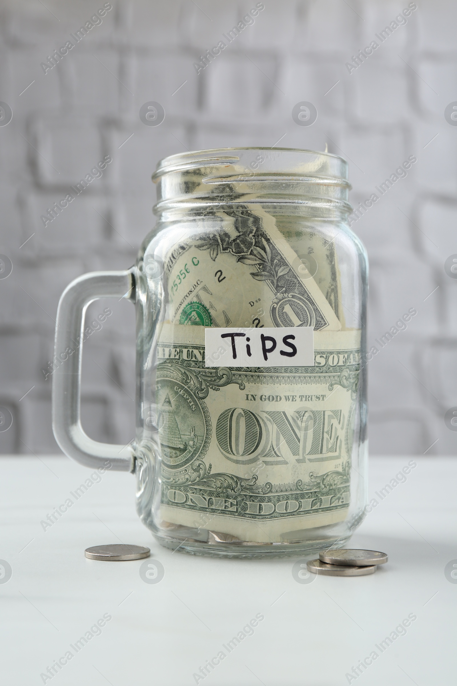 Tips jar with money on white marble table Photo of Tips jar with money on white marble table