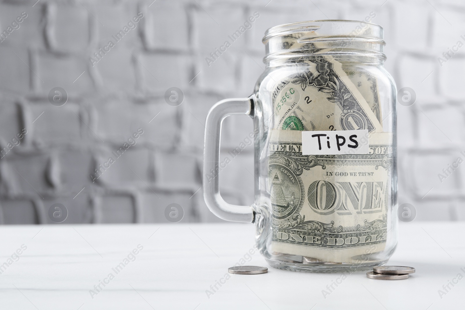Tips jar with money on white marble table, space for text Photo of Tips jar with money on white marble table, space for text
