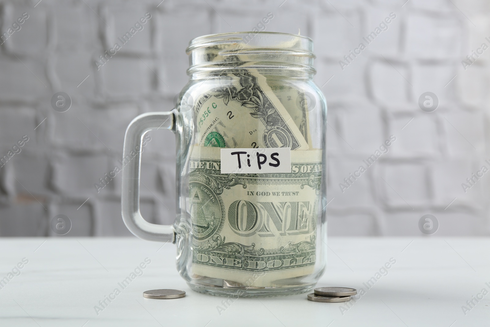 Tips jar with money on white marble table Photo of Tips jar with money on white marble table