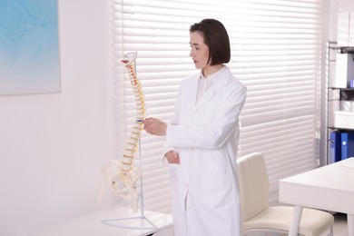 Photo of Doctor pointing at sections of human spine model in clinic