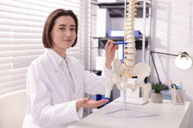 Photo of Doctor pointing at sections of human spine model at desk in clinic