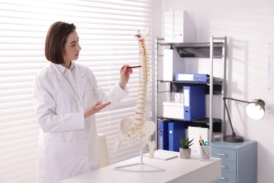 Photo of Doctor pointing at sections of human spine model at desk in clinic