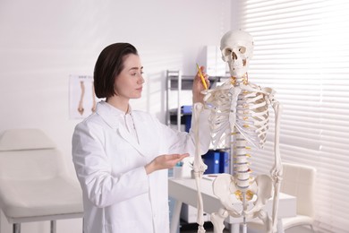 Photo of Doctor pointing at parts of human skeleton model in clinic