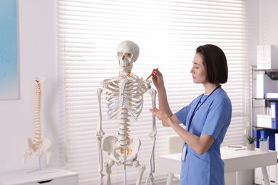 Photo of Doctor pointing at parts of human skeleton model in clinic