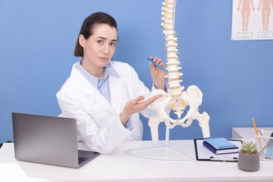 Photo of Doctor pointing at sections of human spine model at desk in clinic