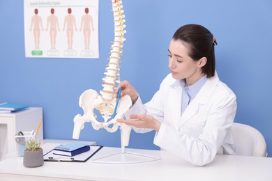 Photo of Doctor pointing at sections of human spine model at desk in clinic