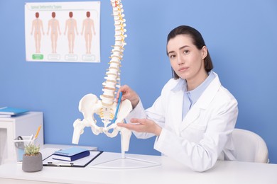 Photo of Doctor pointing at sections of human spine model at desk in clinic