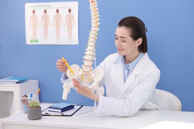 Photo of Doctor pointing at sections of human spine model at desk in clinic