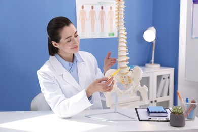 Photo of Doctor pointing at sections of human spine model at desk in clinic