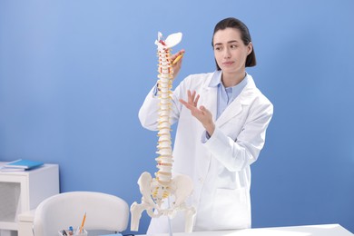 Photo of Doctor pointing at sections of human spine model near blue wall
