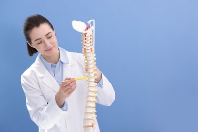 Photo of Doctor pointing at sections of human spine model near blue wall. Space for text