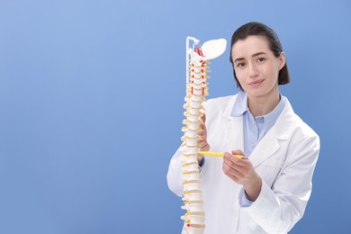 Photo of Doctor pointing at sections of human spine model near blue wall. Space for text