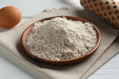Photo of Flour, rolling pin and egg on white wooden table, closeup