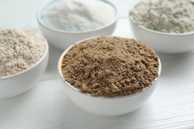 Photo of Different types of flour in bowls on white wooden table, closeup