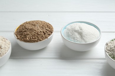 Photo of Different types of flour in bowls on white wooden table, closeup