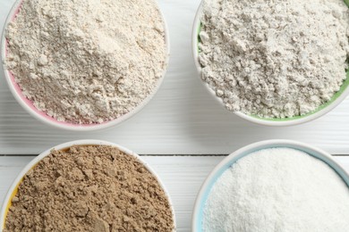 Photo of Different types of flour in bowls on white wooden table, flat lay