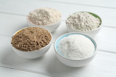 Photo of Different types of flour in bowls on white wooden table, closeup