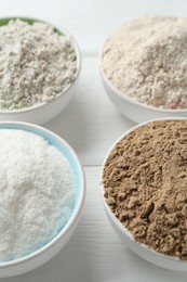 Photo of Different types of flour in bowls on white wooden table, closeup