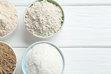 Photo of Different types of flour in bowls on white wooden table, flat lay. Space for text