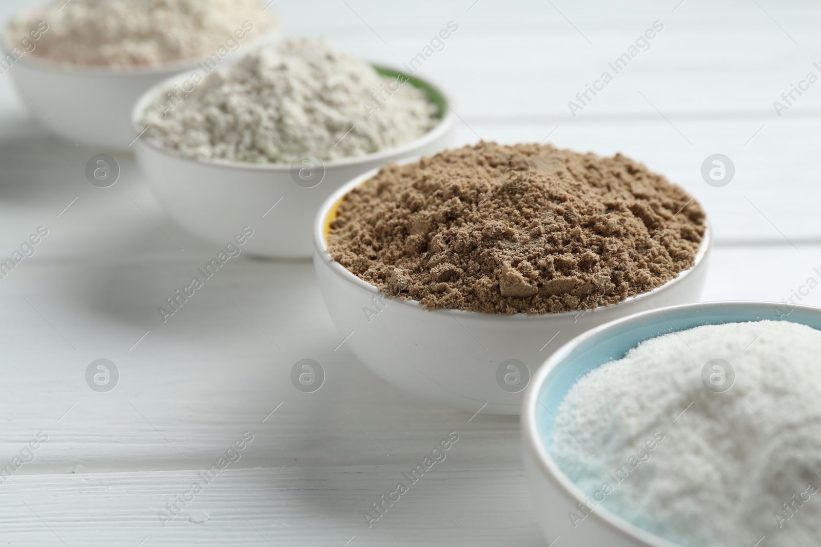 Different types of flour in bowls on white wooden table, closeup Photo of Different types of flour in bowls on white wooden table, closeup