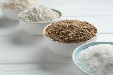 Photo of Different types of flour in bowls on white wooden table, closeup