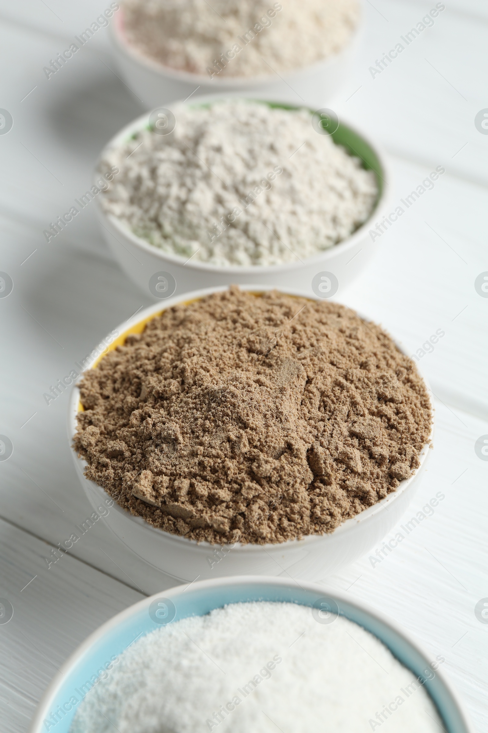 Different types of flour in bowls on white wooden table, closeup Photo of Different types of flour in bowls on white wooden table, closeup