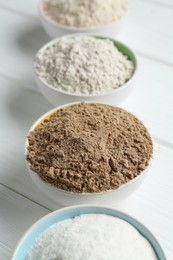 Photo of Different types of flour in bowls on white wooden table, closeup