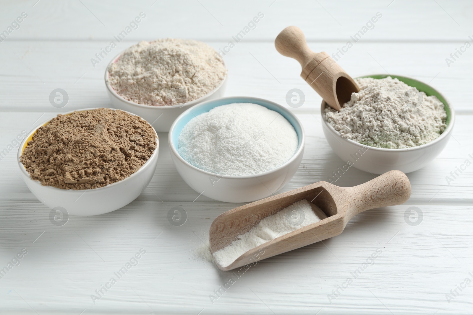 Photo of Different types of flour in bowls and scoops on white wooden table, closeup