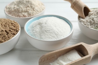 Photo of Different types of flour in bowls and scoops on white wooden table, closeup