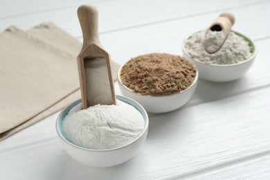 Photo of Different types of flour in bowls and scoops on white wooden table, closeup