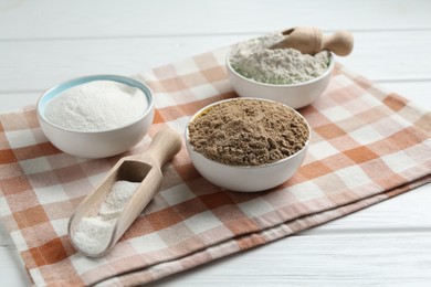 Photo of Different types of flour in bowls and scoops on white wooden table, closeup