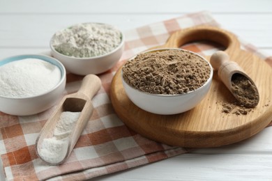 Photo of Different types of flour in bowls and scoops on white wooden table, closeup
