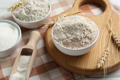 Photo of Different types of flour in bowls, scoop and spikes on table, closeup