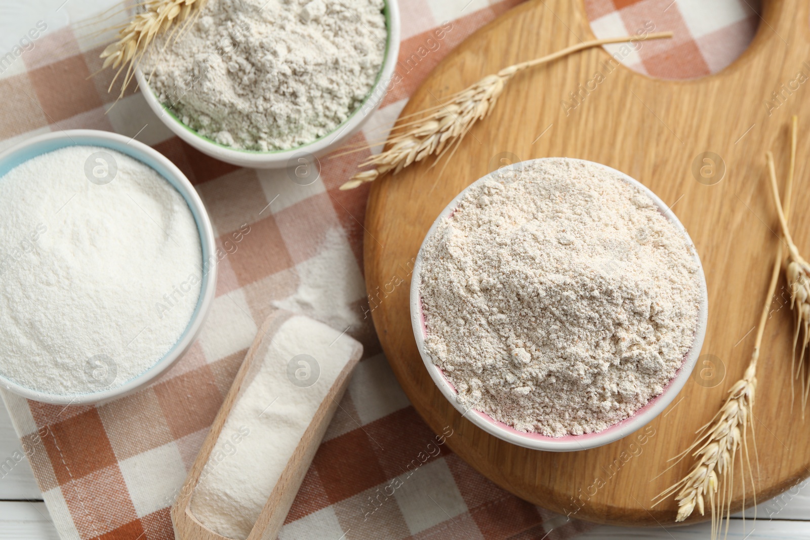 Photo of Different types of flour in bowls, scoop and spikes on table, flat lay