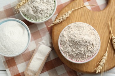 Photo of Different types of flour in bowls, scoop and spikes on table, flat lay
