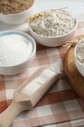Photo of Different types of flour in bowls and scoop on table, closeup