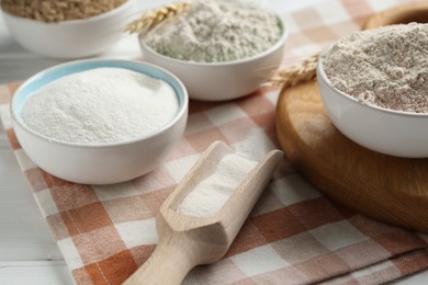 Photo of Different types of flour in bowls and scoop on table, closeup