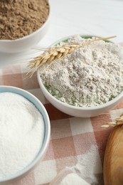 Photo of Different types of flour in bowls and spike on table, closeup